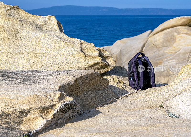 哈尔基季基上,在你的春天徒步旅行。背包和可重复使用的塑料瓶放在海滩附近的岩石上