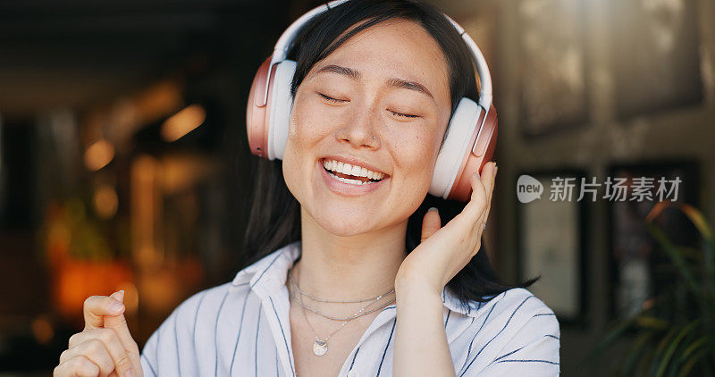 快乐的亚洲女人，耳机和听播放列表的音乐在咖啡馆的音频流媒体，跳舞或唱歌。女性或自由职业者在咖啡馆或餐厅微笑或享受播客，声音或歌曲
