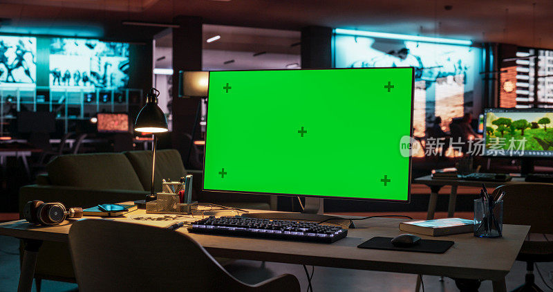 站在霓虹灯照亮的空荡荡的创意办公室的桌子上，模拟绿屏色度键显示的台式电脑。游戏开发或动画公司主管