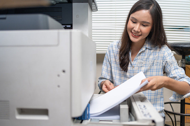 亚洲妇女将纸张插入复印机或影印机以复制文件。