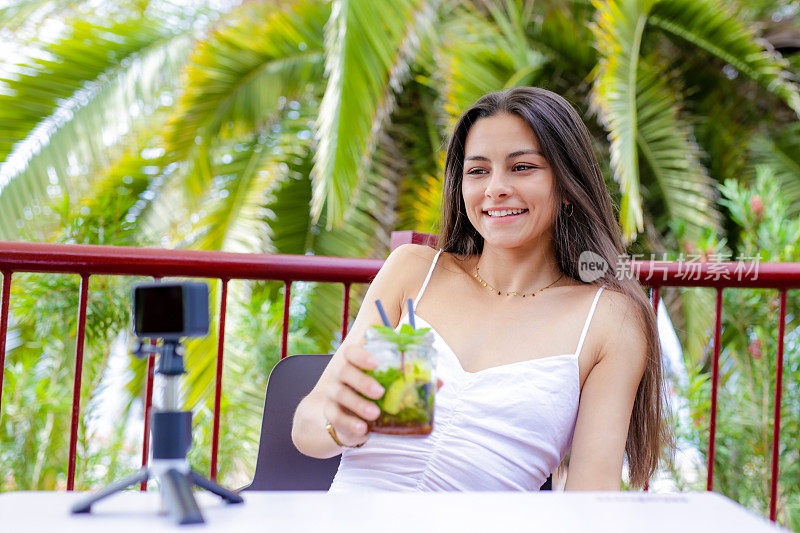 微笑的年轻女子坐在户外露台上为社交媒体创作内容