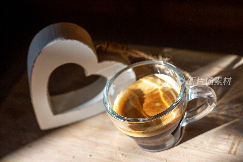 俯瞰透明的意大利浓缩咖啡杯，背后是木制的心。高对比度的早晨厨房照片。背景模糊。自制的早餐。咖啡爱好者概念。壁纸图片