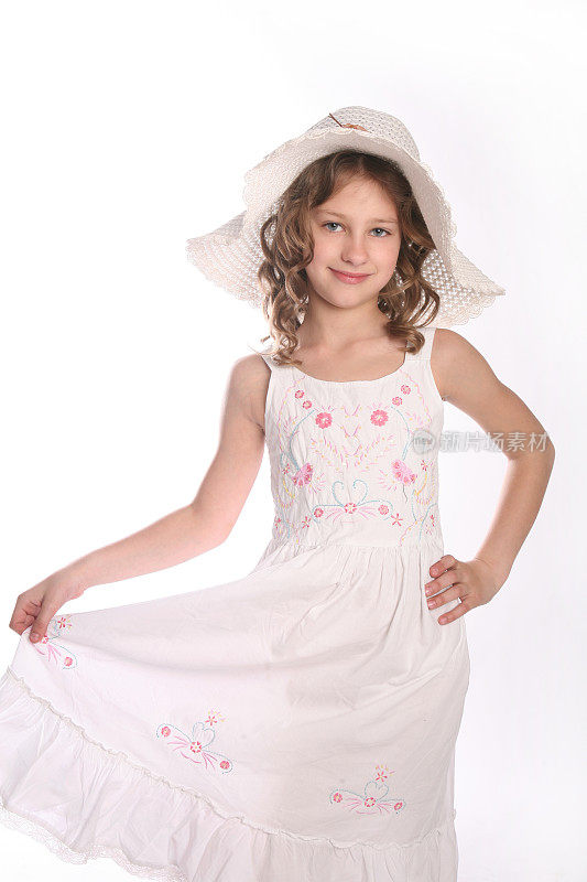 可爱的卷发女孩摆姿势在白色的裙子和帽子