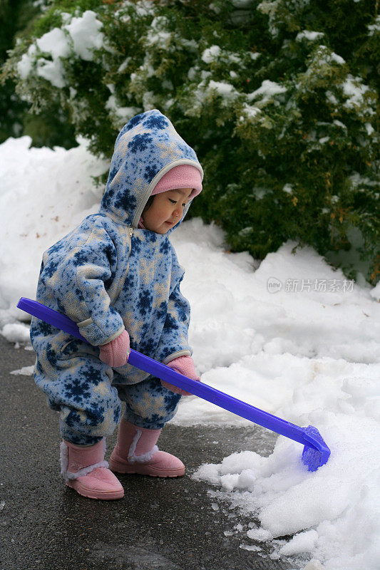 可爱的蹒跚学步的亚洲女孩铲雪和玩雪