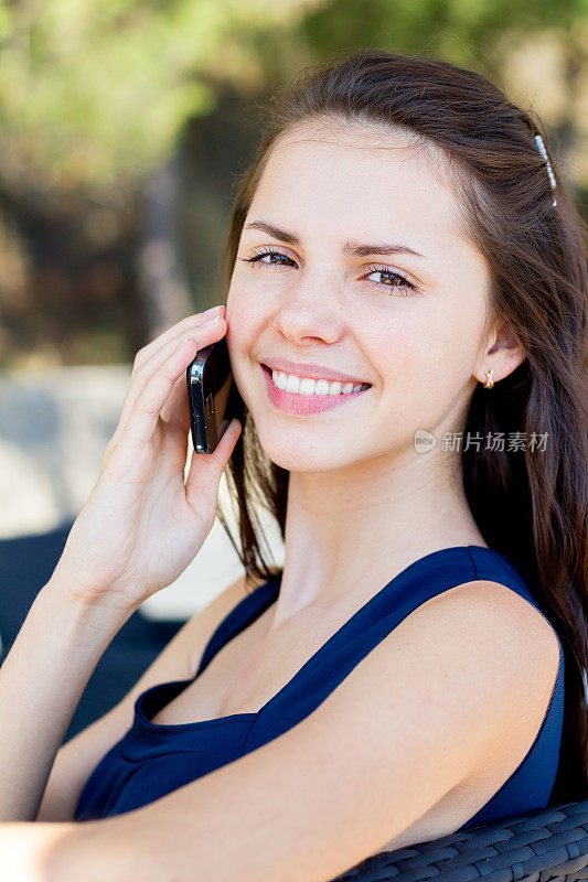 微笑的女孩在户外的咖啡馆里讲手机