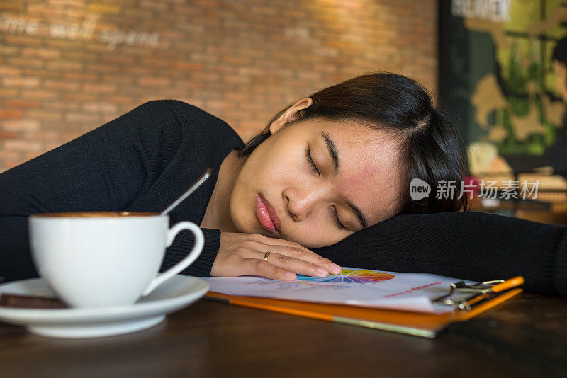 一个亚洲女孩在一杯咖啡旁边的文件上睡着了