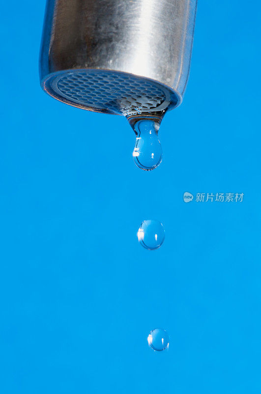 蓝色背景的水龙头上滴下一滴滴水