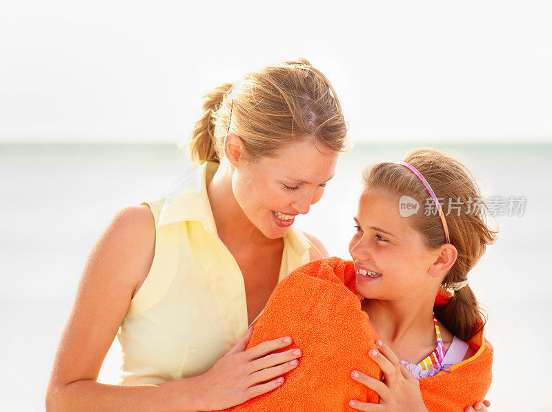 在海滩上，一位慈爱的母亲用毛巾盖住女儿