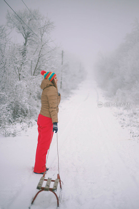 女孩在森林里散步，拉雪橇。一个开心的女人。圣诞假期。女孩免费休息。圣诞树躺在雪橇上。美丽的年轻女孩或女人在森林里散步。拉木制雪橇