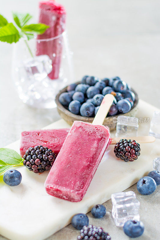 新鲜的夏季野生蓝莓和覆盆子，自制冰沙冰淇淋冰棒在大理石盘子