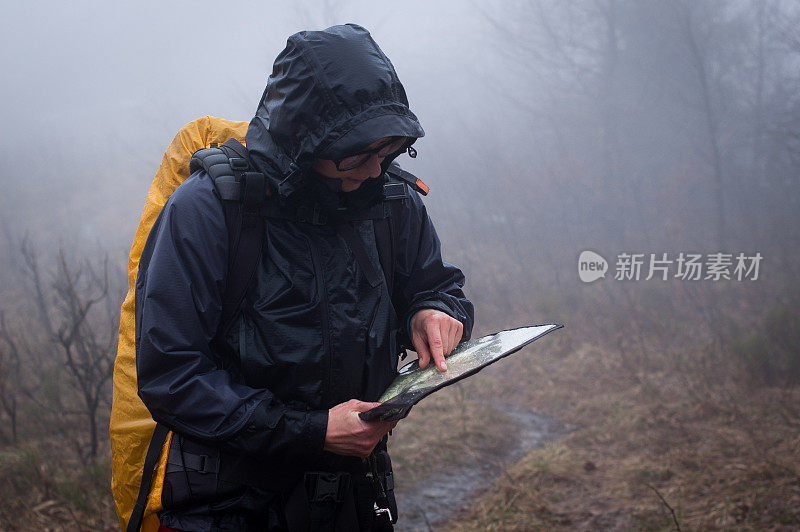 穿着雨衣背着黄色背包的人在雾中查看地图