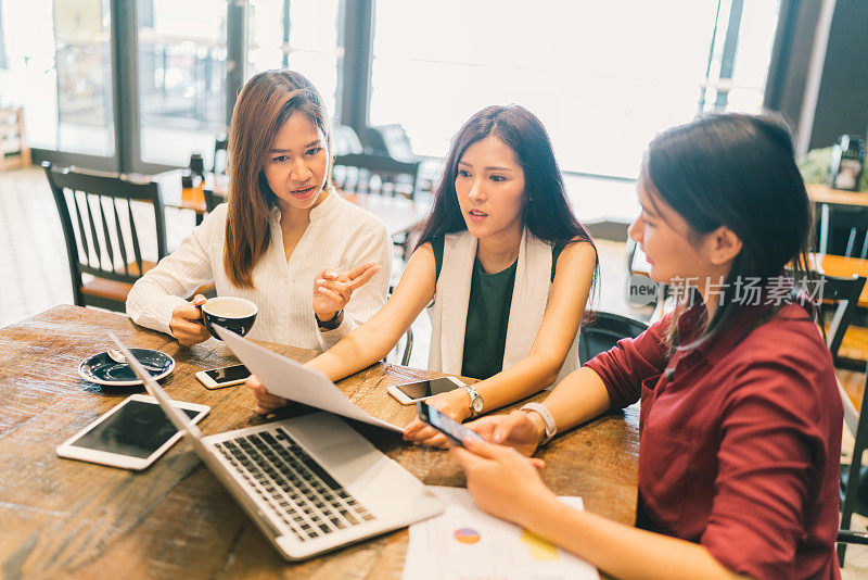 一群年轻的亚洲女性或大学生在咖啡馆参加严肃的商务会议或项目头脑风暴讨论。有笔记本电脑，数字平板电脑和智能手机。创业或团队合作理念。
