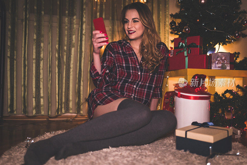 迷人的女人在圣诞节期间在家使用手机