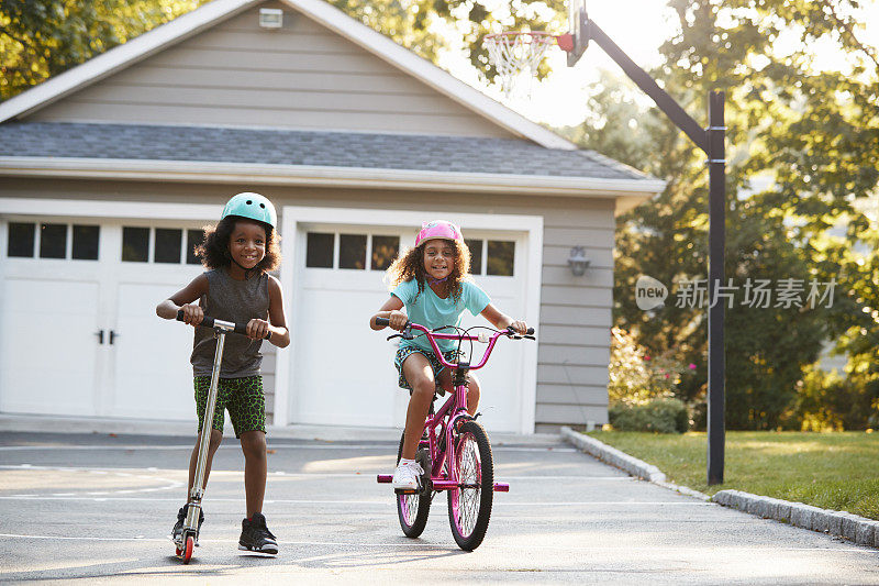 姐姐和哥哥在家里的车道上骑摩托车和自行车