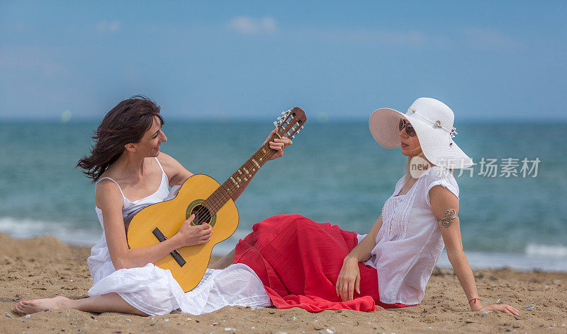 两个快乐的成熟女人微笑着在海滩上弹吉他