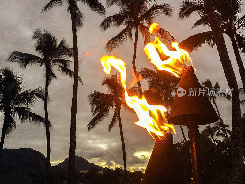 夏威夷海滩上点燃的提基火炬，以山为背景