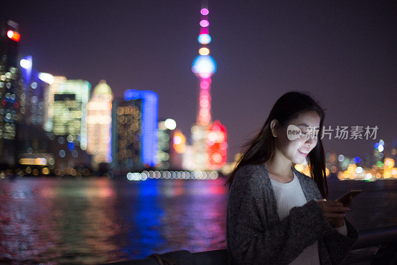 年轻的亚洲妇女在现代城市玩手机