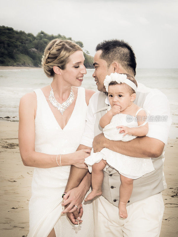 新娘和新郎在海滩上抱着宝贝女儿亲吻
