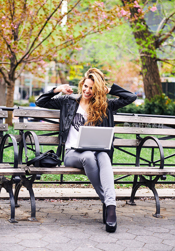 美丽的女孩坐在公园里，膝盖上放着笔记本电脑，玩得很开心，美国纽约联合广场