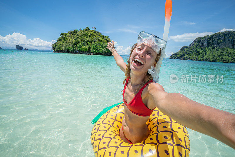 一名年轻女子在泰国群岛清澈的海水中与充气菠萝在田园诗般的海滩上自拍。人们旅行奢侈，乐趣和酷的态度概念