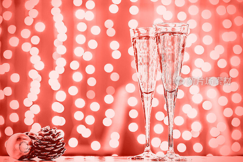 两杯香槟和圣诞玩具。节日灯光散景背景。紫外光色调，2018年度流行色。活珊瑚主题——2019年度色彩