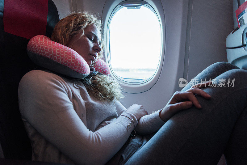 一位女乘客在飞机上睡在颈垫上。
