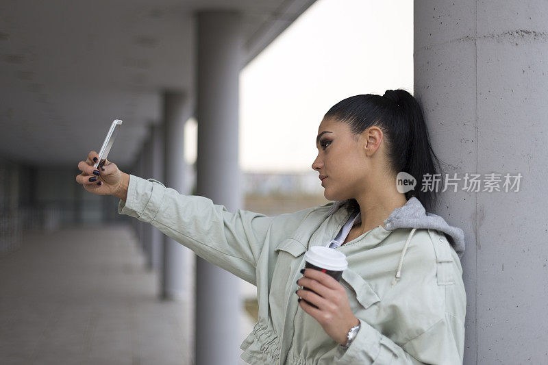 年轻女孩在户外喝着咖啡，拿着电话。