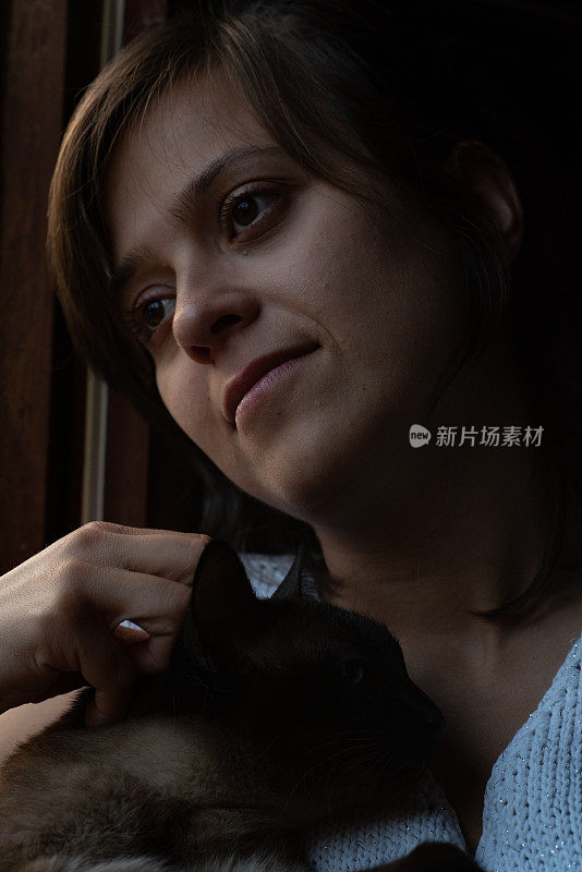 一个漂亮的女人从窗户往外看，还带着猫