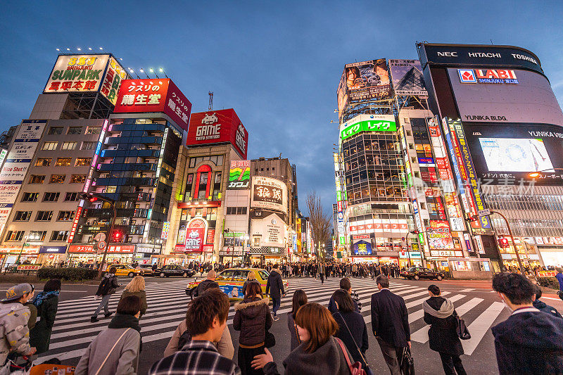 新宿镇晚上的街道上挤满了等待人行横道的人。新宿是位于东京的一个夜间购物区。