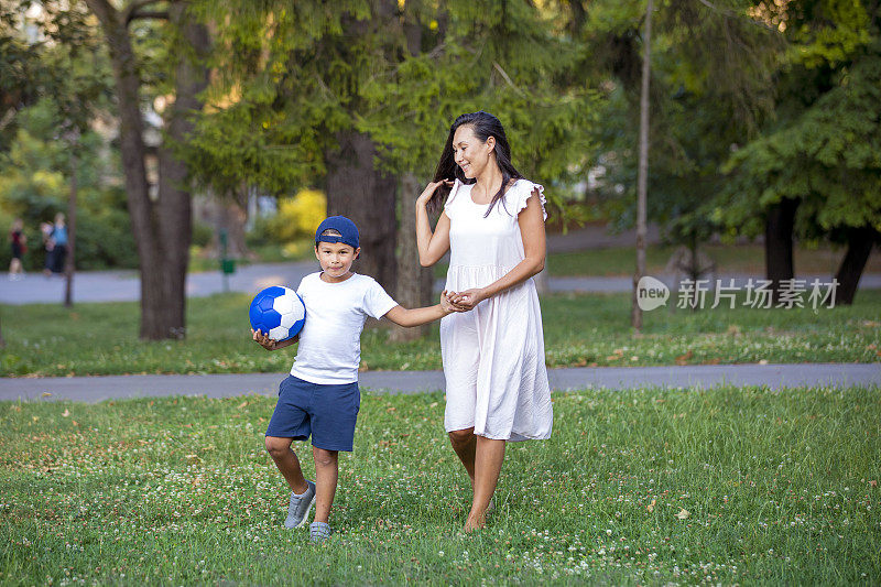 一位母亲正在公园里和她的儿子玩球。亚洲母亲和儿子踢足球