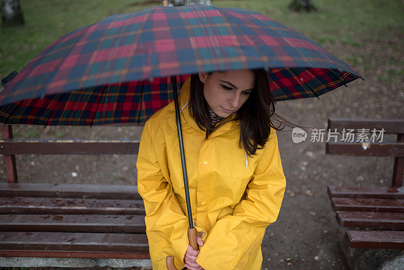 穿着黄色雨衣的年轻女子在公园里度过雨天