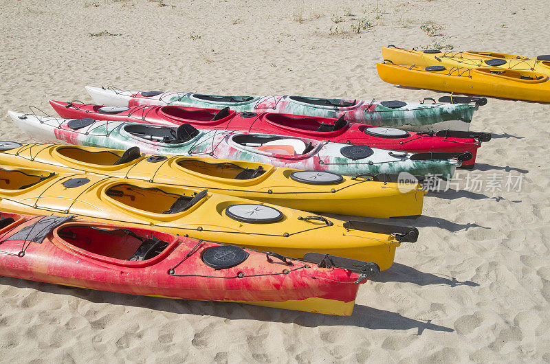 在阳光明媚的日子里，沙滩上有许多五颜六色的双人海上皮划艇