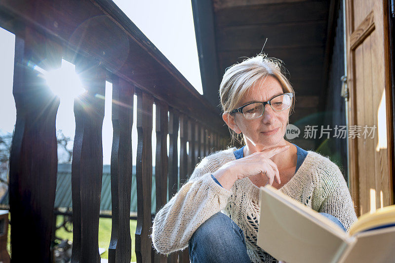 一个女人在阳台上放松，看书，享受秋高气爽的周日下午