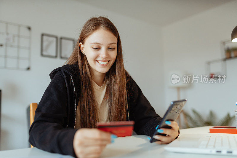 女学生在家学习，穿着帽衫，使用笔记本电脑。用信用卡在网上购物的女人