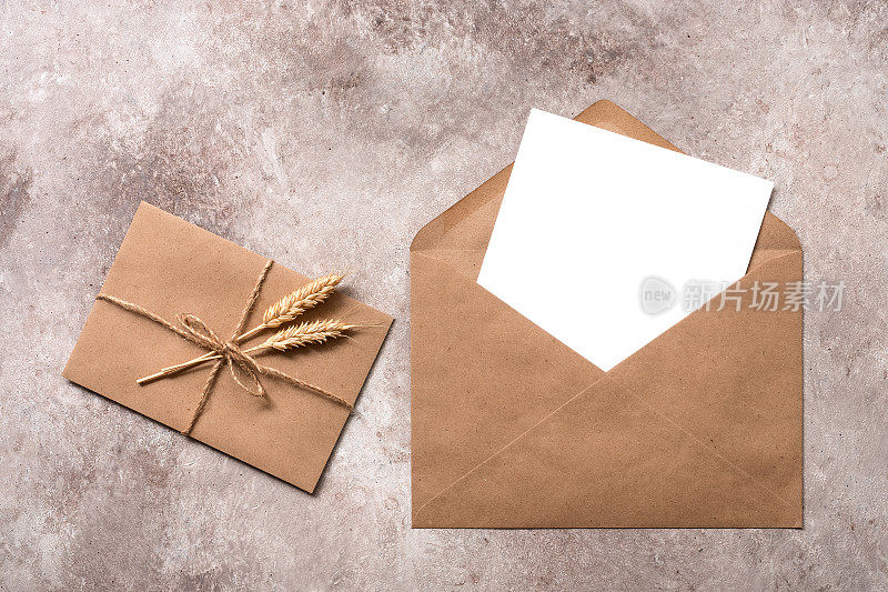 空白纸卡模型在一个工艺棕色信封。用麻绳绑着熟透的小麦穗的古老信件。邀请模板。米色枯燥乏味的背景。俯视图，平放。
