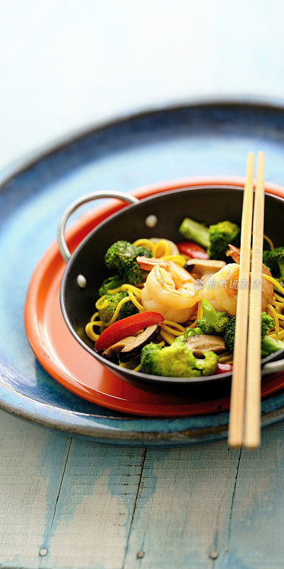 新鲜的亚洲炒虾与蔬菜和面条在一个个人服务的锅，筷子放在锅上。