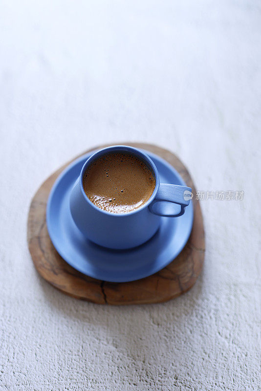 土耳其起泡咖啡在一个蓝色陶瓷杯，浅灰色的混凝土地板上的木制过山车，特写