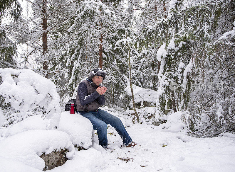 这个人感到冷了，就用热咖啡暖暖身子。一个中年白人男子走在冬天的森林里。步行旅游。