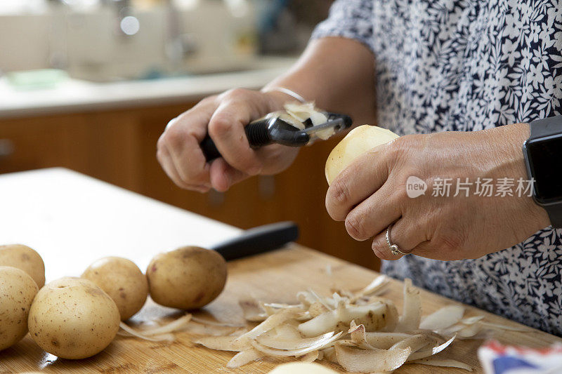 在一个家庭厨房里，女性的手在木制砧板上削土豆