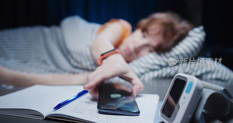 成熟的女人从电话中醒来，从床头柜上拿起她的智能手机，把她的血压监测器和笔记本放在旁边