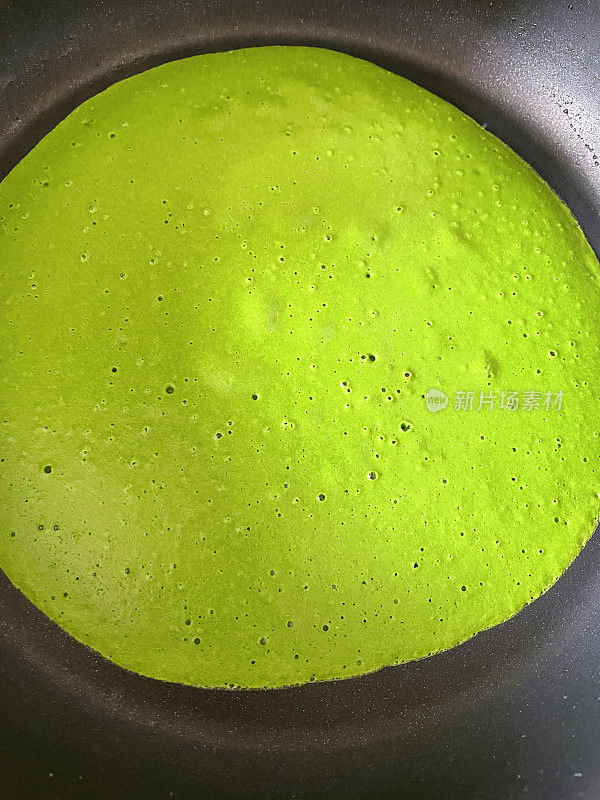一个不粘锅的特写图片，里面有冒泡的绿色菠菜面糊，正在自制煎饼