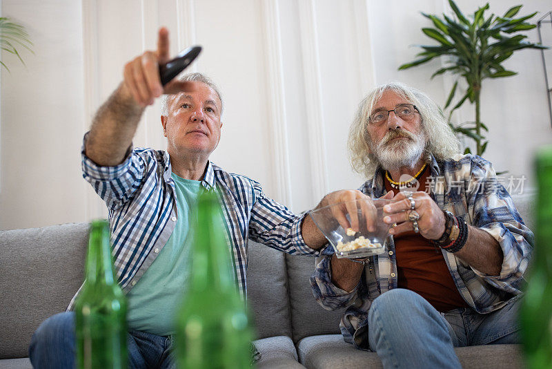 两个年长的男性朋友在客厅边喝啤酒边吃爆米花边看电视