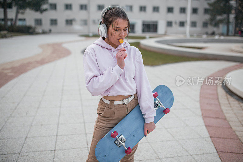 年轻女子拿着棒棒糖在公园里玩滑板享受音乐