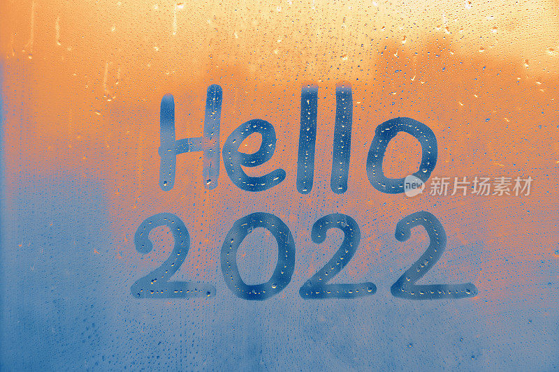 在蓝色和日落的窗户上用手指泼洒着雨蒙蒙的玻璃上写着Hello和数字2022的新年彩绘