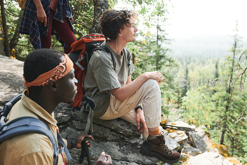 一群年轻的多民族徒步旅行者站在山上的大石头上，欣赏周围的自然美景