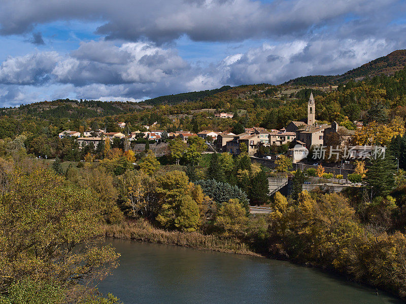在法国普罗旺斯的Sisteron镇北部，在杜兰斯河的秋日里，教堂和传统的房屋被五颜六色的树木包围着。