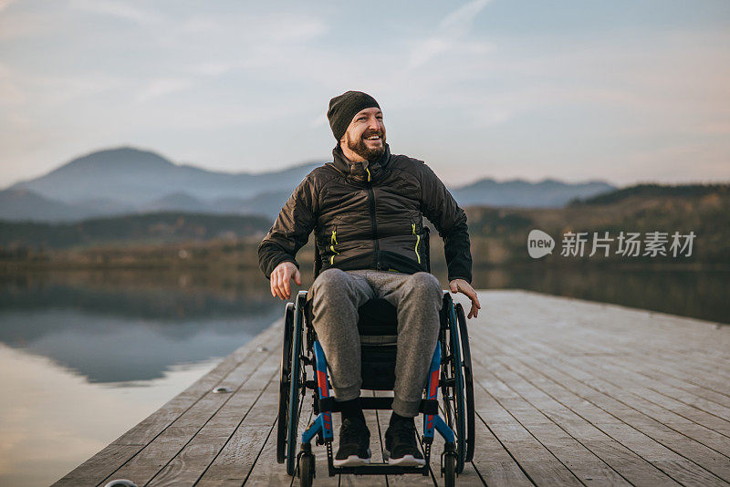 夕阳西下，坐在轮椅上的微笑的残疾人坐在湖边的码头上