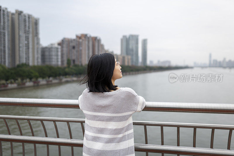 在市中心的一座桥上，一位亚洲妇女望着远方