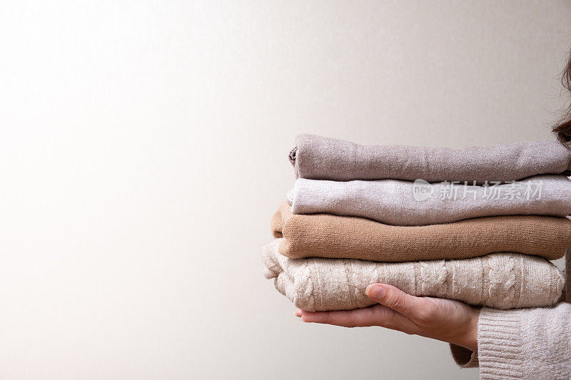 堆叠舒适的针织毛衣在女性手中的米色背景。温暖的概念