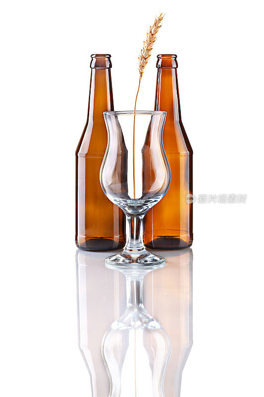 两个空啤酒瓶，一个啤酒杯和麦穗的静物。工作室拍摄与自然反射隔离在白色背景上。